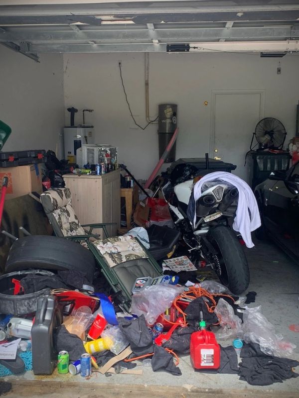 Cluttered garage with motorcycle, tools, and various items scattered around.