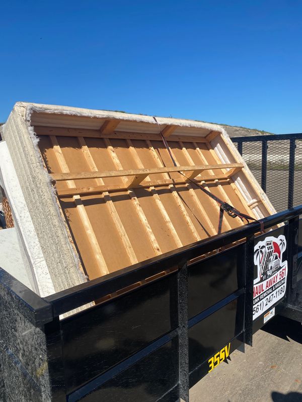 Old mattress frame loaded in a black hauling trailer under clear skies.
