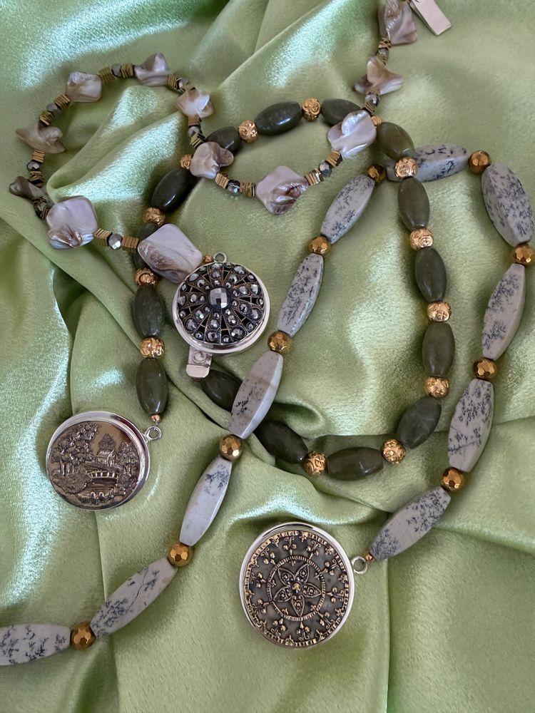 Decorative beaded necklaces with intricate pendants displayed on green fabric.