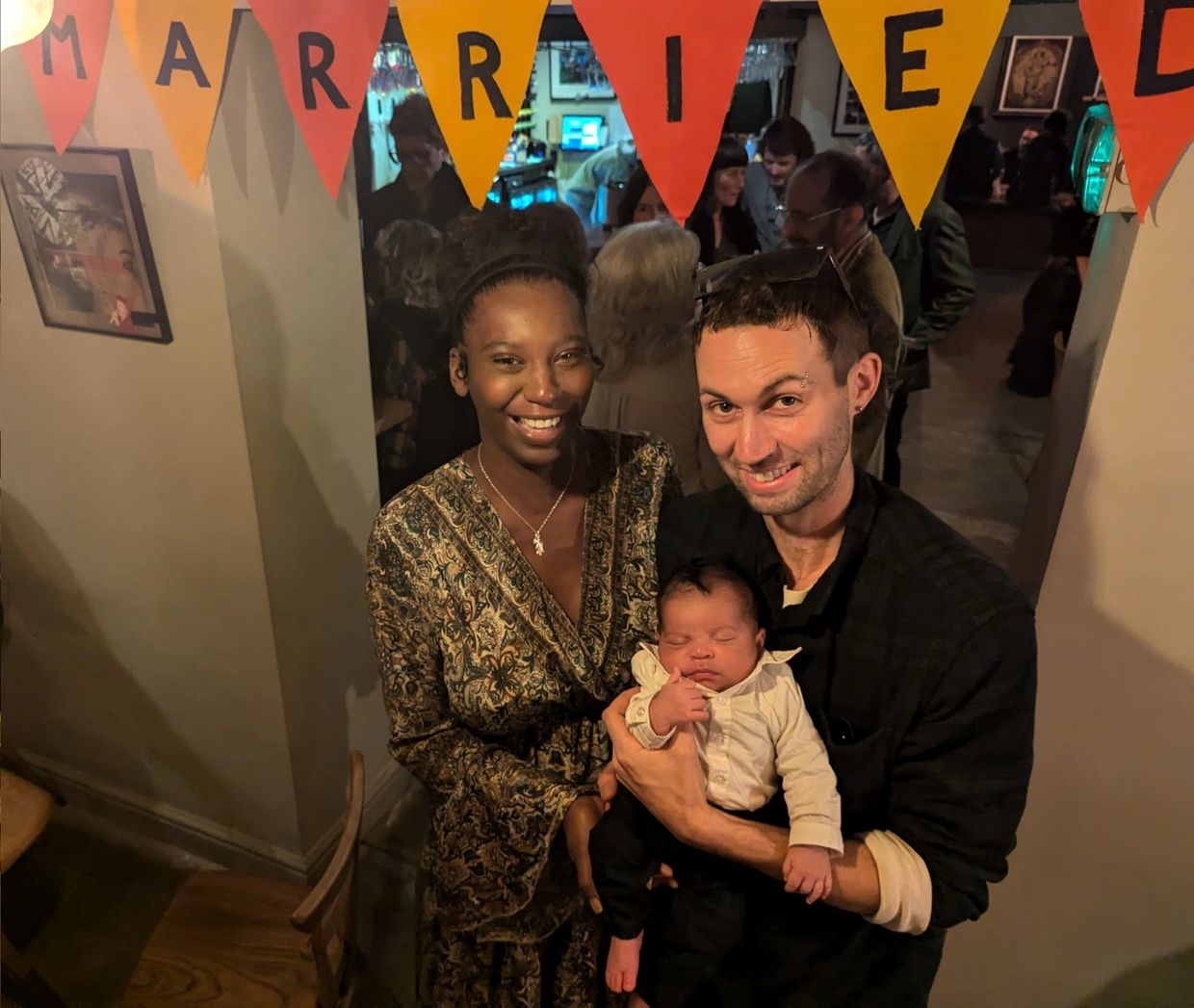 A happy couple holding their baby under a "Married" banner at a celebration.
