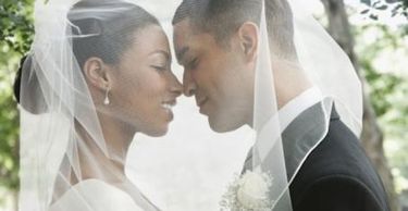 Bride and groom touching foreheads under a veil.