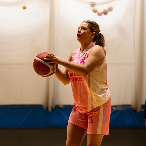 Female basketball player preparing for a shot in pink uniform.