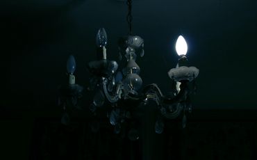 A dark room with a chandelier, one bulb glowing.