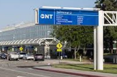 Airport terminal entrance with directional signage and vehicles.