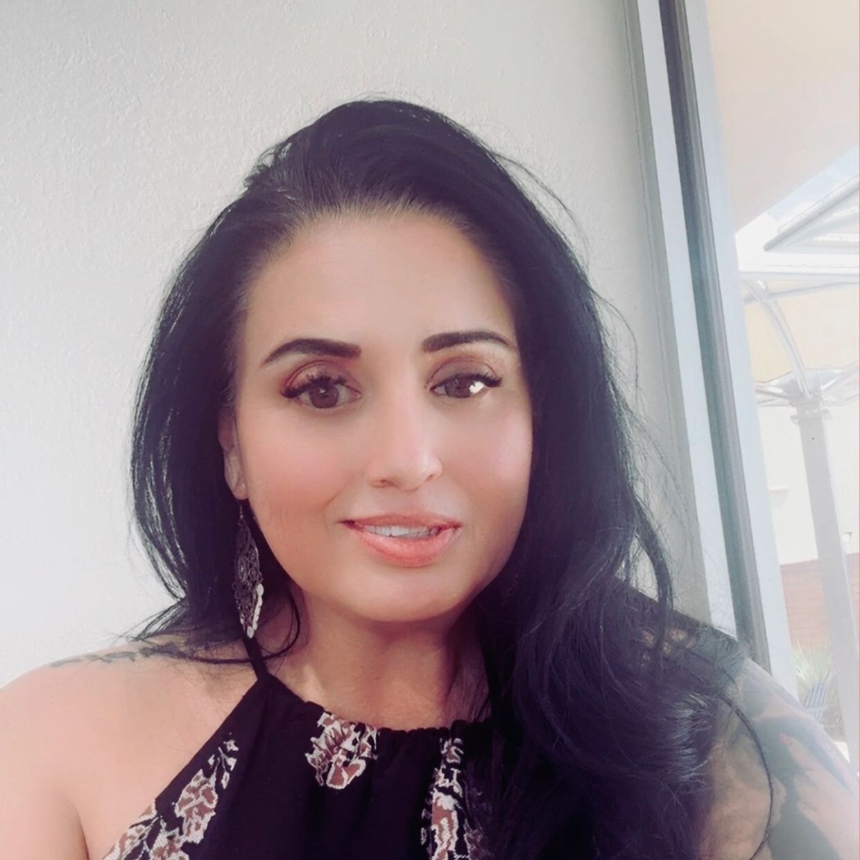 Woman with long black hair smiling indoors near a window.