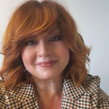 Smiling woman with red hair wearing a checkered blazer.