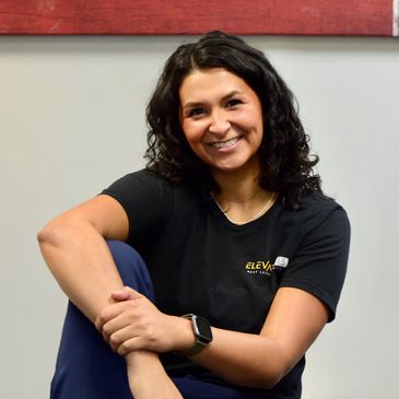 Smiling woman with dark curly hair in casual attire.