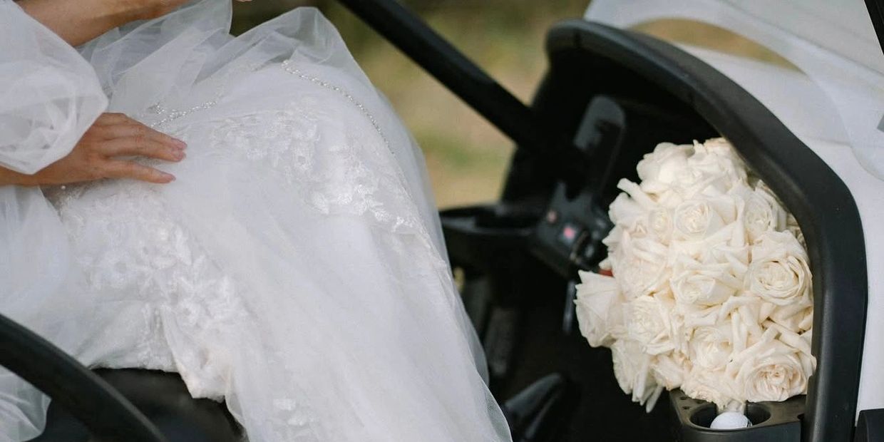 Bride in white gown with bouquet in golf cart.