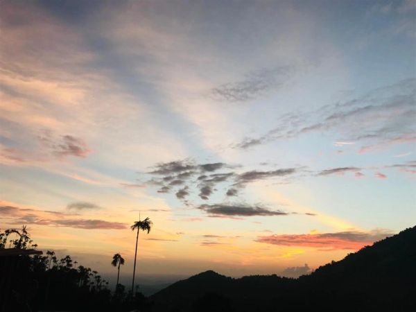 Sunset over silhouetted hills and palm trees with a colorful sky.