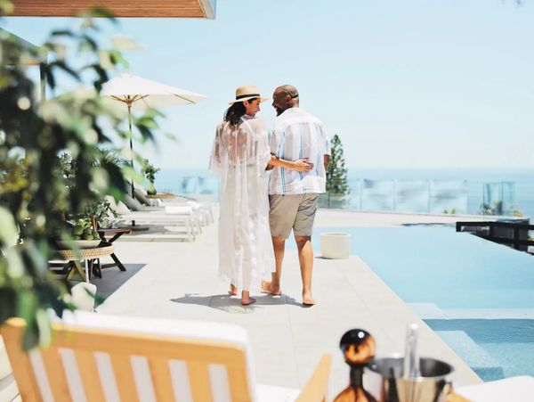 Couple walking by a luxurious pool overlooking the ocean on a sunny day.