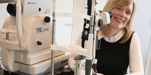 Fran the optometrist smiling beside optical machinery.