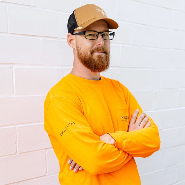 Man in bright orange long sleeve shirt and brown cap with glasses.