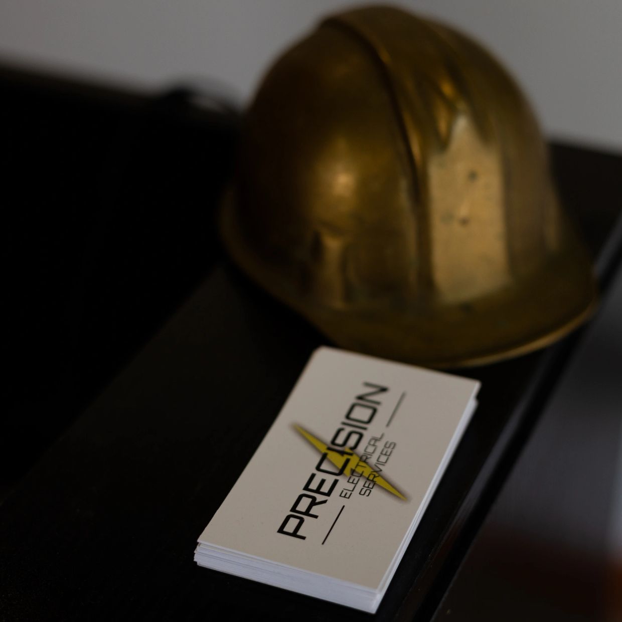 Business cards for Precision Electrical Services next to a brass hard hat.