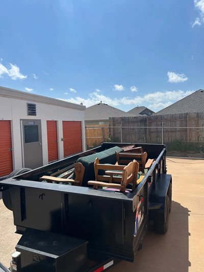 A trailer filled with discarded furniture outside storage units on a sunny day.