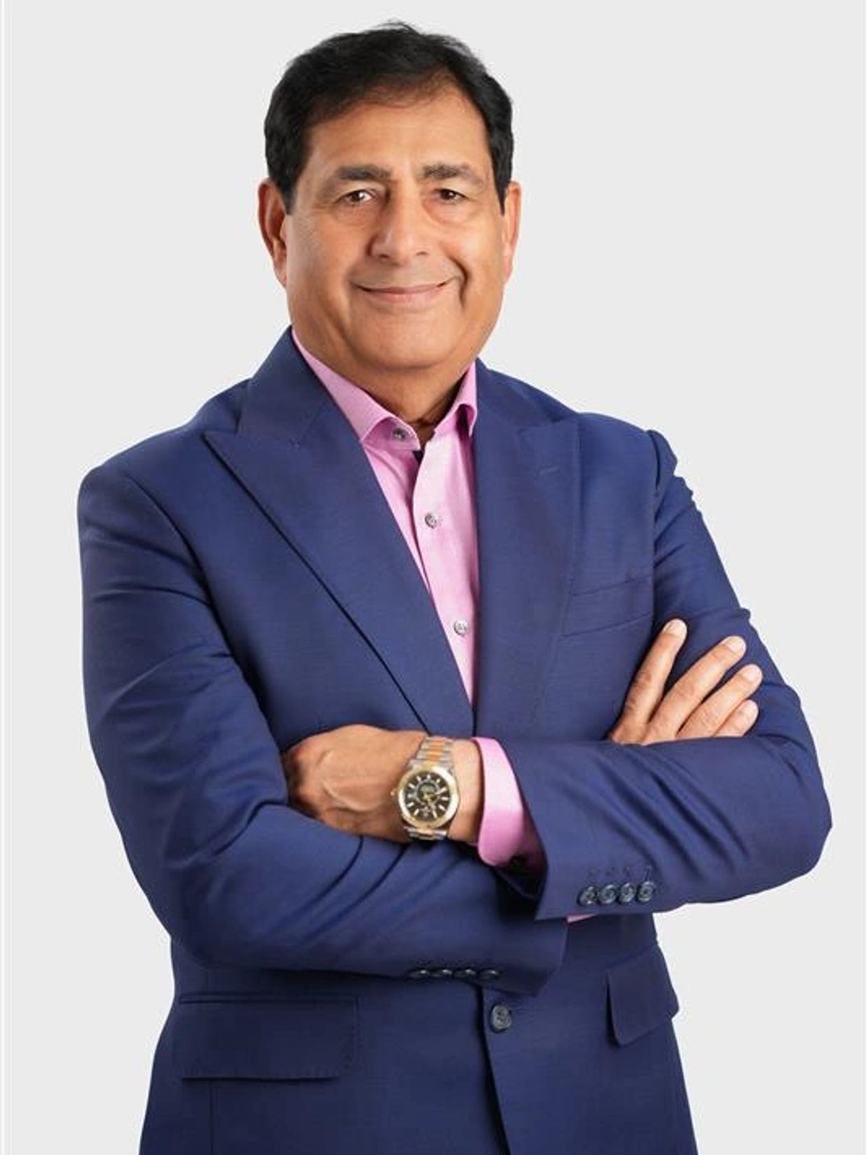 Confident man in blue suit with arms crossed, smiling.