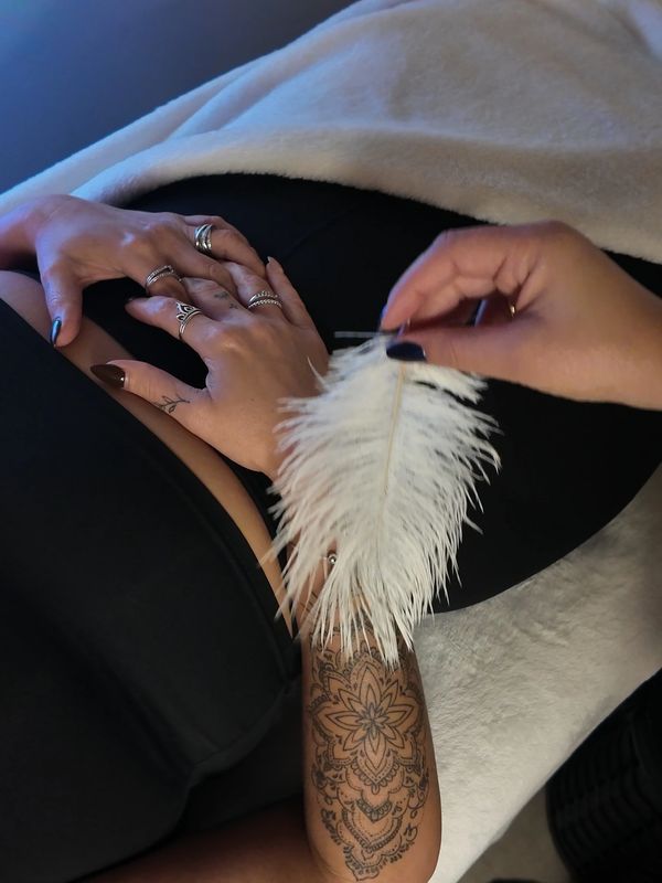 Person with tattooed arm gently touching another's hands with a white feather.