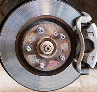 Close-up of a car brake disc and caliper with some rust on the hub.