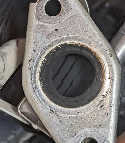 Close-up of a metal car part with a circular opening and some dirt around it.