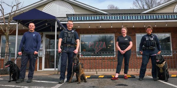 Four people with three police dogs outside a pizza restaurant.