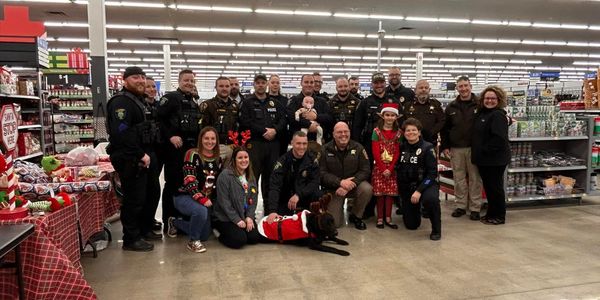 Group of police officers, civilians, and a dog posing in a store with holiday decorations.