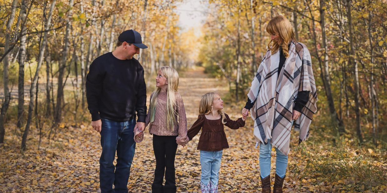 Family holding hands on a leaf-covered path in autumn woods.