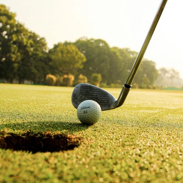 Golf club poised to hit a ball near the hole on a sunny course.