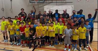 Large group of kids and coaches posing in a gym with soccer uniforms.