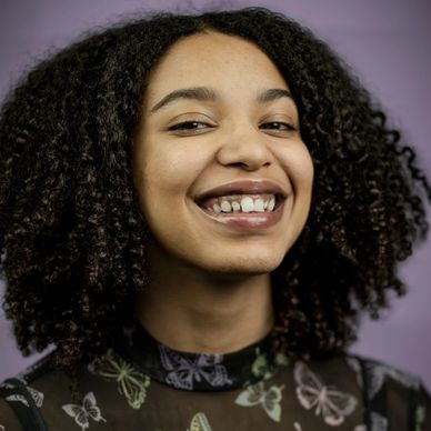 Smiling woman with curly hair against a purple background.