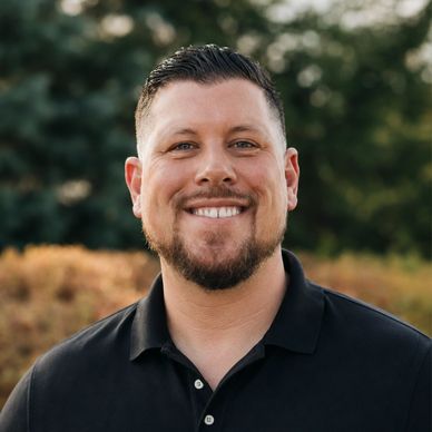 Smiling man with short hair and beard outdoors.