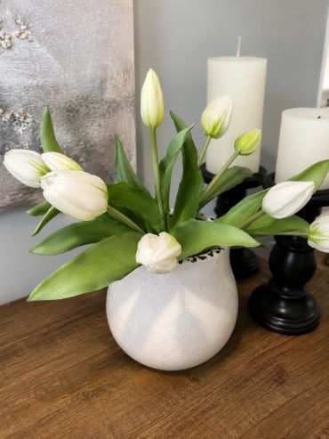 White tulips in a white vase on a wooden table.