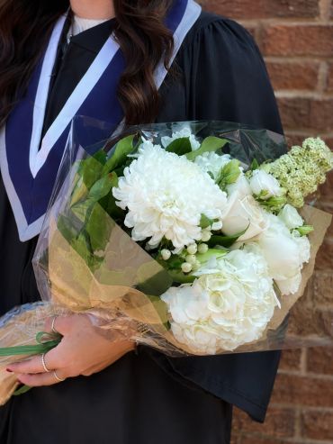 Person in graduation gown holding a bouquet of white flowers.