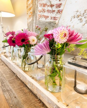 Vases with pink flowers arranged on a wooden tray.