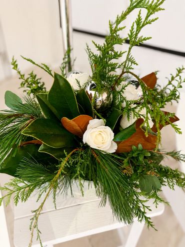 Festive floral arrangement with greenery and white rose.