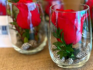 Red rose in a glass jar with pine cones.