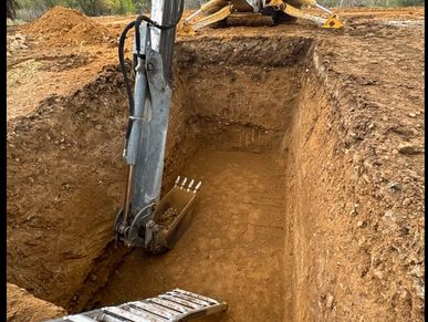 Excavator digging a deep rectangular hole with a ladder inside.