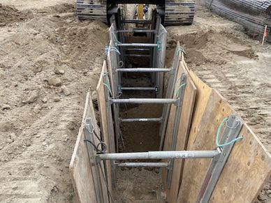 CAT excavator digging a trench with safety shoring in place at a construction site.
