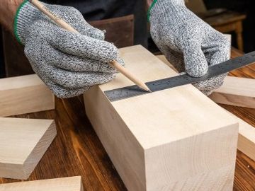 Person marking wood with pencil and ruler wearing gloves.