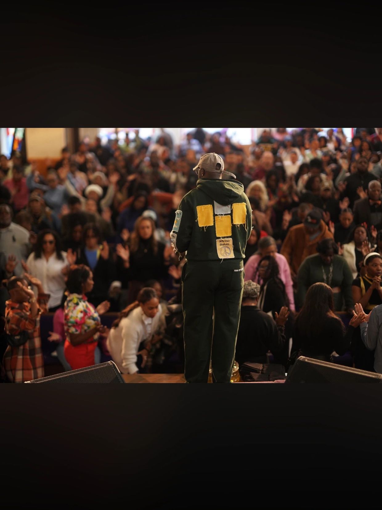Person on stage addressing a large, engaged audience in a gathering or event.