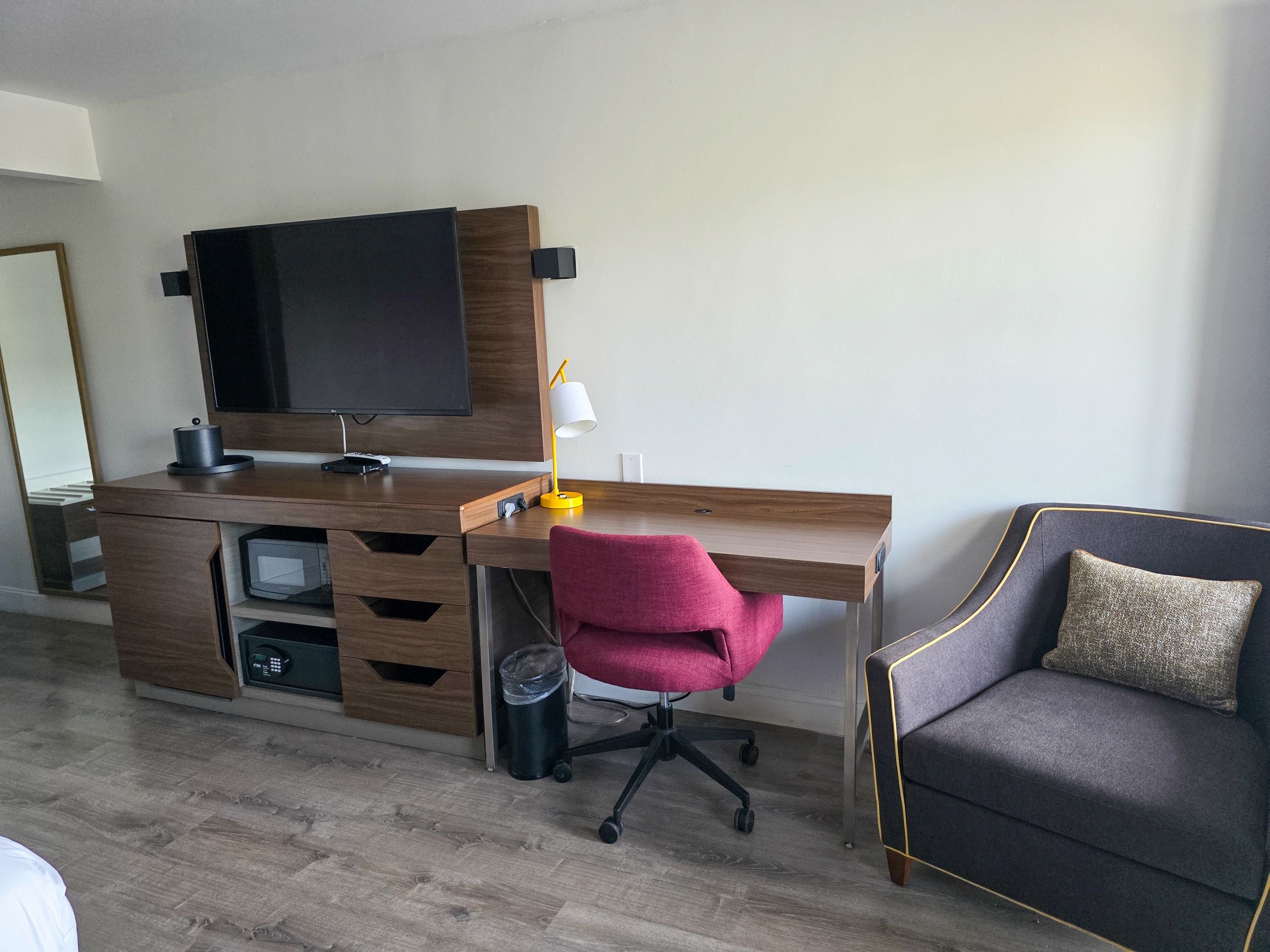 Modern hotel room corner with TV, desk, chair, and sofa.