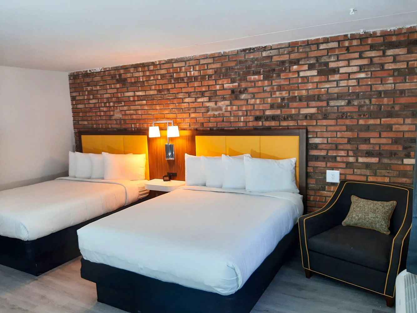 Two beds with yellow headboards against a brick wall in a modern hotel room.