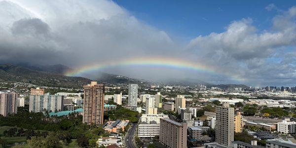 A vibrant rainbow arches over a cityscape with mountains and clouds.