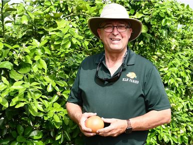Smiling man in a hat holding an onion in front of lush green foliage.