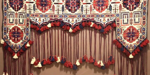 Intricately patterned textile with red, blue, and white tassels hanging from the edges.