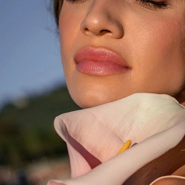 Close-up of a woman's lips and chin with a white flower near her neck.