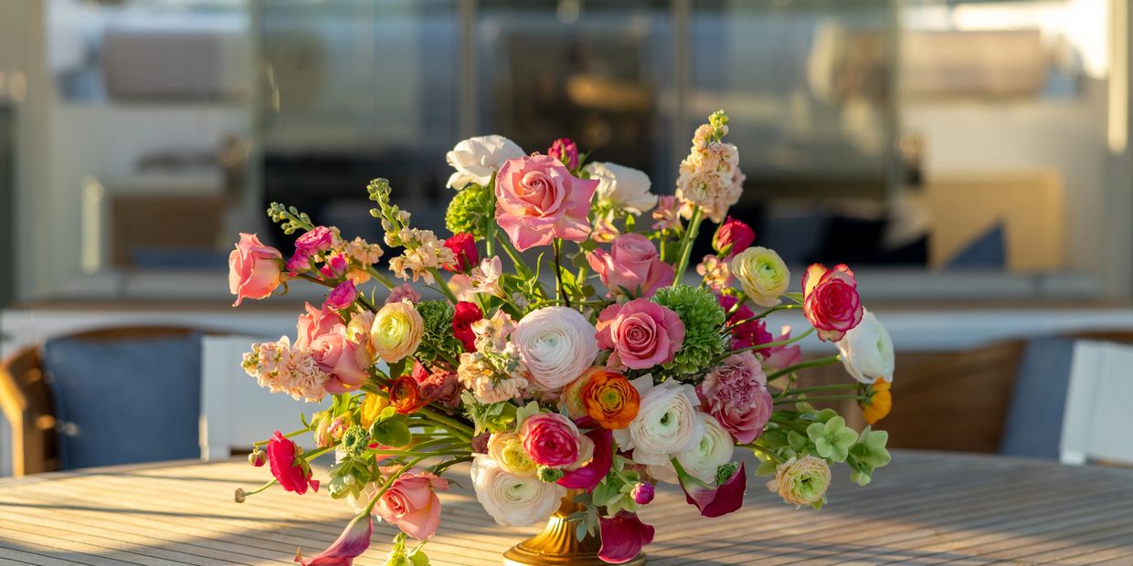 A vibrant bouquet of mixed flowers on a wooden table in sunlight.