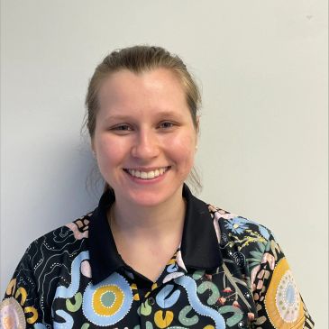 Smiling woman wearing a colorful patterned shirt against a plain background.