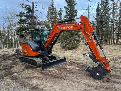 Orange Hitachi excavator parked on a dirt clearing near trees.