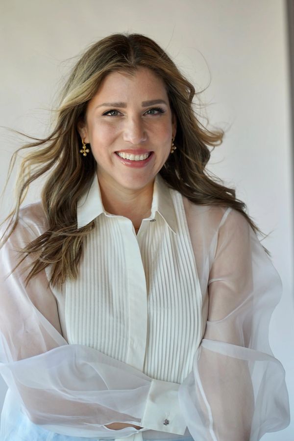 Smiling woman with wavy hair in a sheer white blouse.