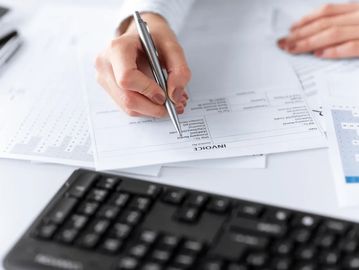 Person filling out an invoice form with a pen near a keyboard.