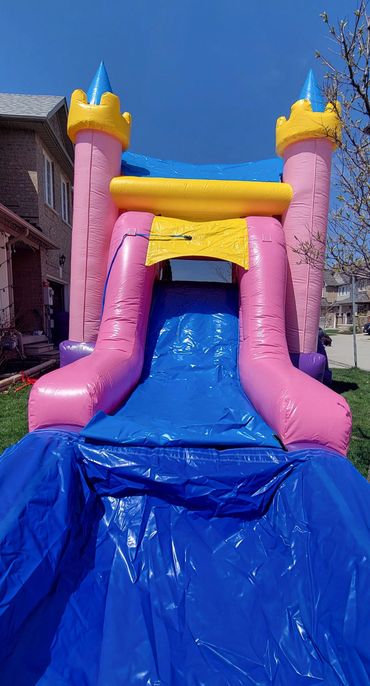 Colorful inflatable castle slide set up in a backyard under a clear blue sky.